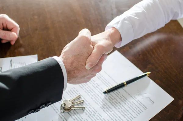 Poignée de main au-dessus d'un contrat signé, d'un stylo et de clés